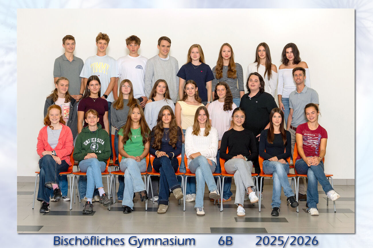 Eine Klasse von Schülern und ein Lehrer stellen sich in drei Reihen für ein Gruppenfoto auf.