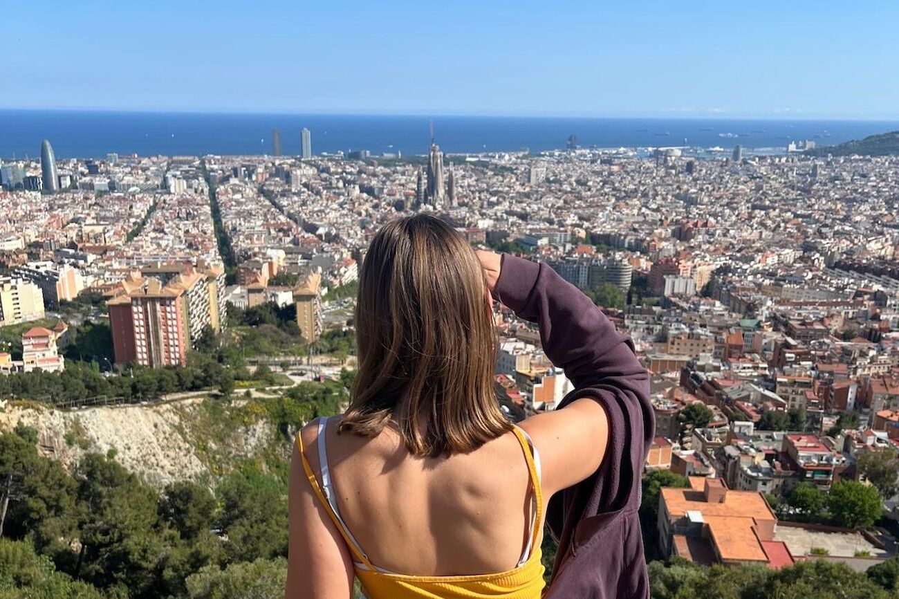 Frau mit Blick auf eine Stadtlandschaft und das Meer in der Ferne an einem sonnigen Tag.