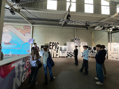 Menschen betrachten moderne Kunstplakate in einer Galerie im industriellen Stil.