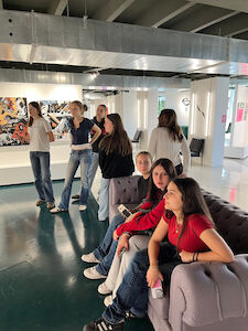 Eine Gruppe junger Menschen sitzt und steht in einer modernen Kunstgalerie.