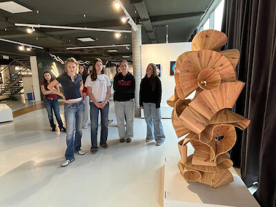 Fünf Personen betrachten eine große abstrakte Holzskulptur in einer Kunstgalerie.