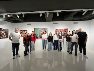 Eine Gruppe von Menschen posiert in einer Kunstgalerie mit Blumengemälden an den Wänden.