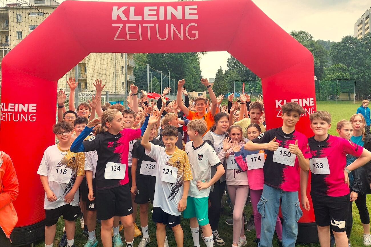 Eine Gruppe von Kindern in Startnummern versammelt sich unter einem roten Bogen bei einer Laufveranstaltung.