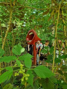 Kinder gehen an einer großen roten Skulptur in einem üppigen grünen Garten vorbei.