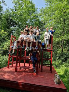 Eine Gruppe von Kindern sitzt auf übergroßen roten Stühlen in einem üppigen, grünen Außenbereich.