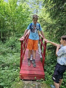 Zwei Jungen auf einer kleinen roten Brücke in einem üppigen grünen Wald.