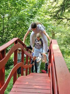 Ein Kind springt über ein anderes auf einer roten Brücke in einer grünen, bewaldeten Gegend.