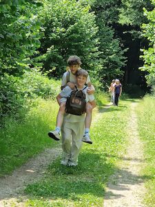 Ein Junge nimmt einen anderen Jungen auf einem Waldweg huckepack.